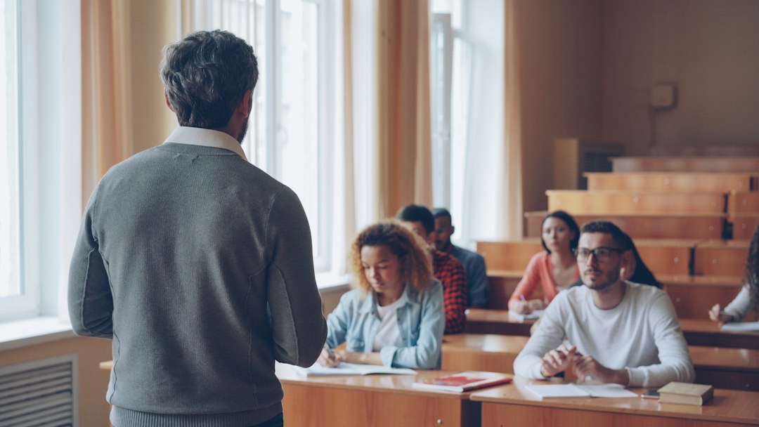 Teacher instructs diverse students in a sunlit lecture hall.